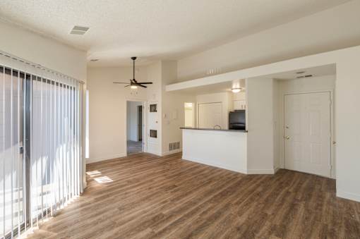 A living room with a ceiling fan and a kitchen area in the background.
