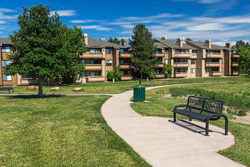 A park with a bench and a pathway leading to apartment buildings.