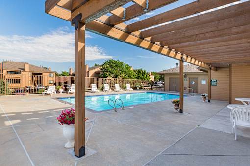 A pool area with a wooden pergola and a white chair.