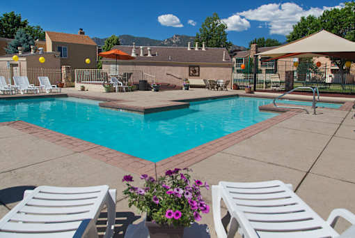 A pool surrounded by white chairs and a patio umbrella.