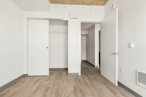 A room with white walls and wooden flooring with two open doors.