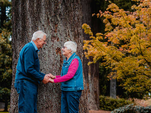 An elderly couple holding hands in front of a tree.