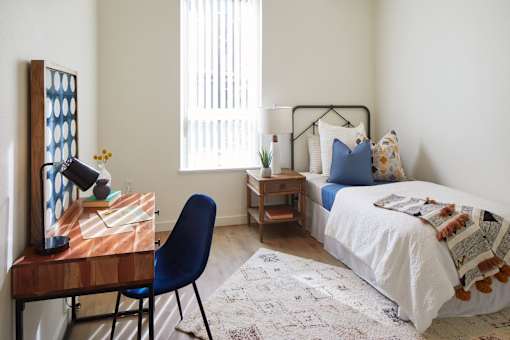 A blue chair sits in front of a desk with a lamp and a vase of flowers.