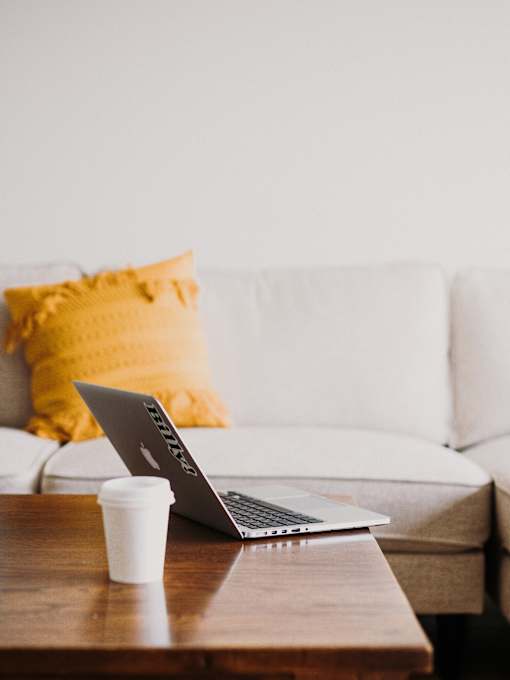 a laptop on a coffee table with a white couch and yellow pillows in the background