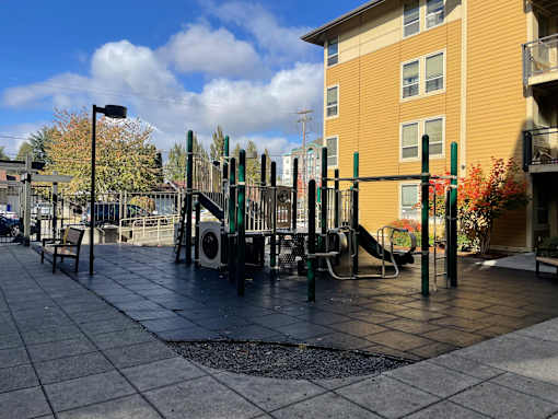 A playground with a slide and swings in front of a yellow building.