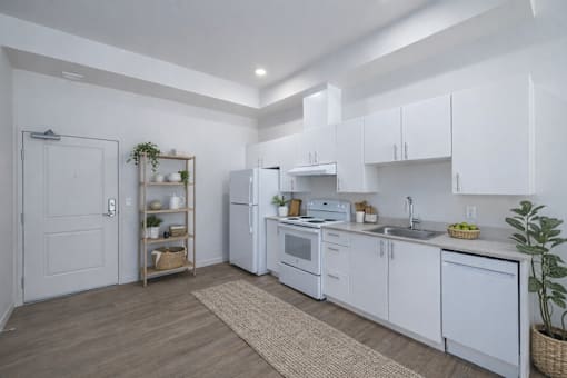 A kitchen with white cabinets and appliances, a wooden floor, and a rug on the floor.