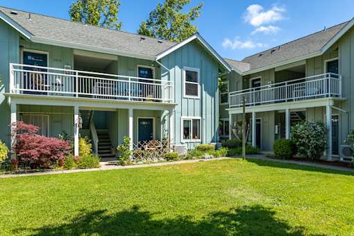 A green and white two story apartment building with a green lawn in front.