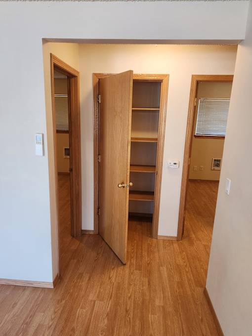 A room with a wooden floor and a white wall with a door open.