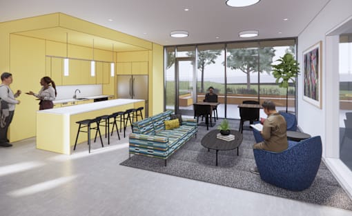 A modern kitchen with a yellow wall and people standing and sitting around it.