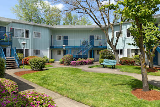 A tree in a grassy area in front of a building with blue staircases.