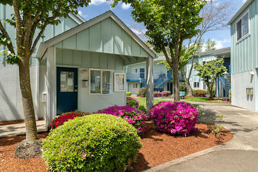 A small building with a blue door is surrounded by greenery and flowers.