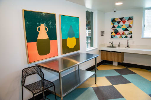 a room with a table and two paintings on the wall and a sink