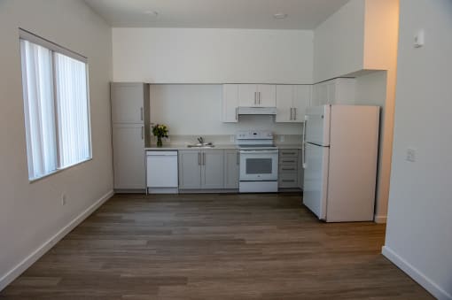 an empty kitchen with white appliances and a window