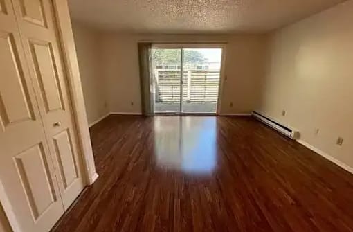 A room with wooden floors and a sliding glass door leading to a balcony.
