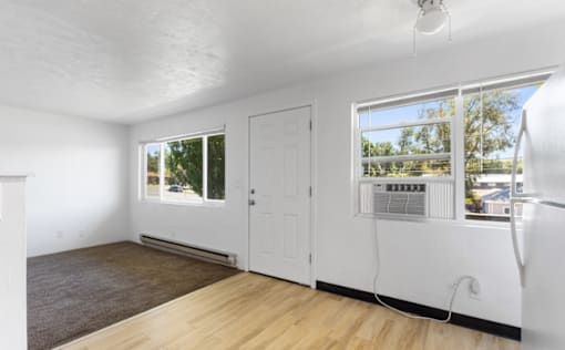 A room with a white door, a window with a view of trees, and a ceiling fan.