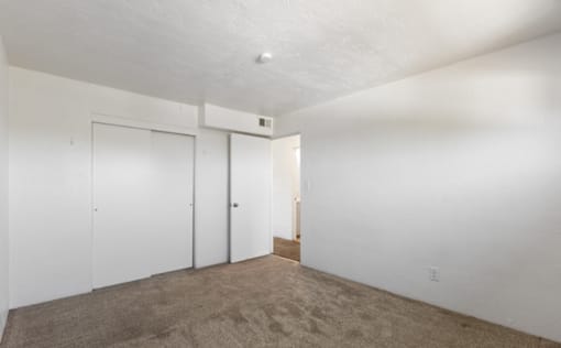 A room with white walls and carpeted floor with two doors.