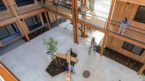 A man and a woman are sitting on a bench in a courtyard surrounded by wooden buildings.