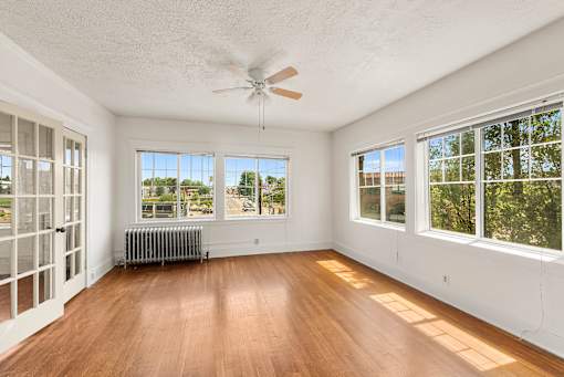 A room with a ceiling fan and large windows.