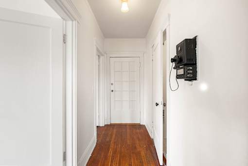 A hallway with a door on the left and a wall-mounted TV on the right.