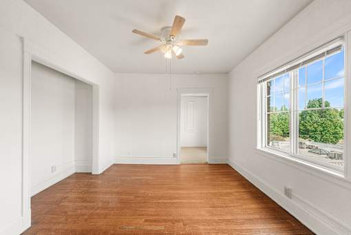 A room with a ceiling fan and a window overlooking a street.