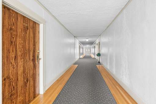 A long hallway with a wooden door on the left and a carpeted floor.