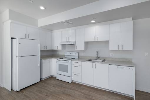 A white kitchen with a refrigerator, stove, oven, and sink.