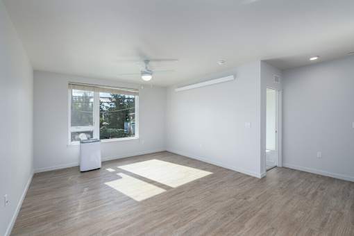 A room with a ceiling fan and a window with a view of trees and a trash can.
