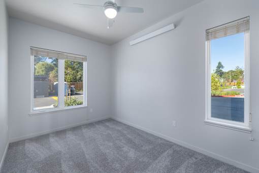 A room with a ceiling fan and two windows.
