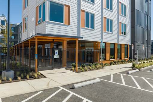 A modern building with a grey and orange facade is surrounded by a parking lot.