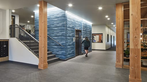 A woman walks down a hallway with a blue stone wall on the side.