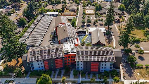 A modern building with a red and white facade is surrounded by trees and other buildings.