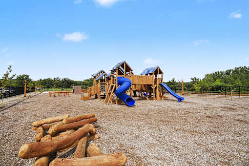 A playground with a blue slide and wooden logs on the ground.