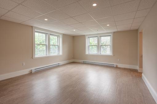 A spacious room with wooden floors and two windows.