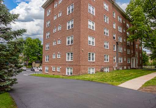 A tall red brick building with many windows and a driveway in front.