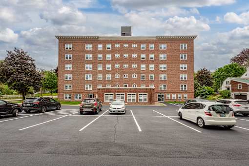 A parking lot in front of a red brick building with cars parked.