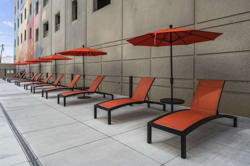 a row of orange lounge chairs with red umbrellas in front of a building at The Icon, Richmond, VA 23230