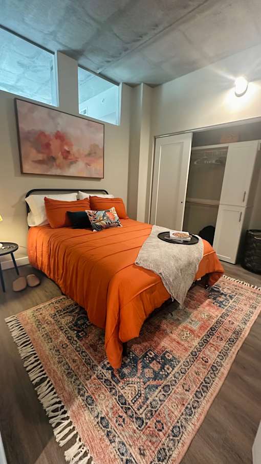 A bedroom with a bed covered in an orange bedspread and a rug on the floor.