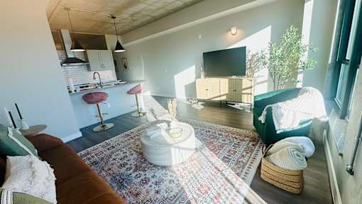 A living room with a rug, a couch, a television, and a kitchen area in the background.
