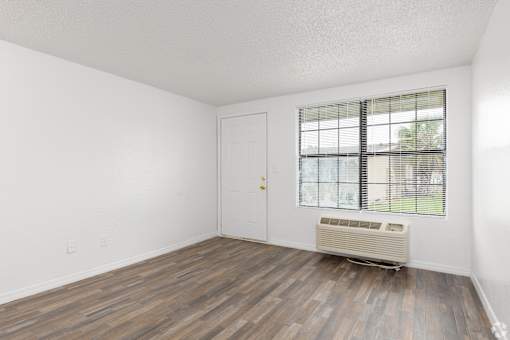 A room with a wooden floor and a window with blinds.