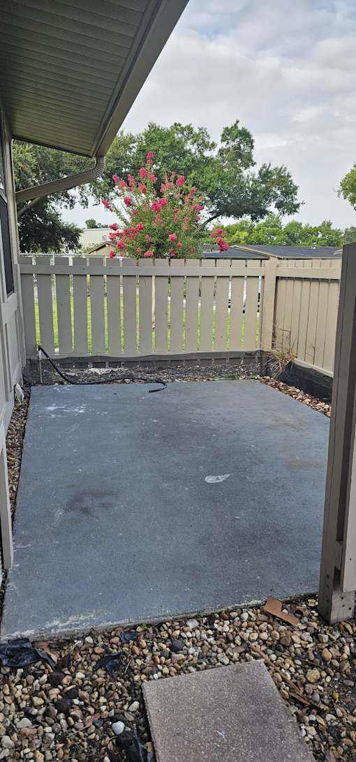 A concrete patio with a white fence and a red flowering bush in the background.