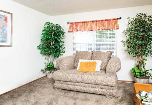 A couch with a yellow pillow is in front of a window with a red curtain.