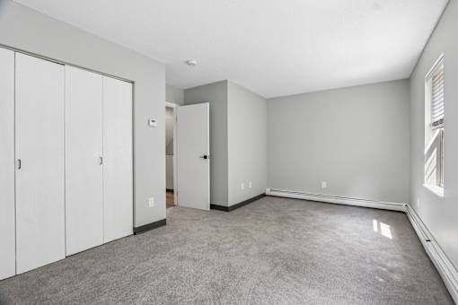 A room with grey carpet and white walls with a white door and a white wardrobe.
