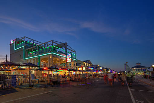A group of people are walking on a street with a building with a green neon sign on it.