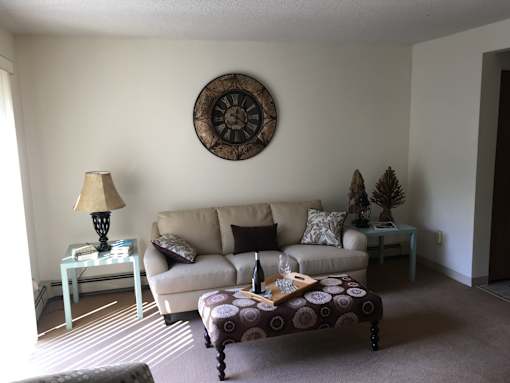 A living room with a couch, a table with a lamp, and a clock on the wall.