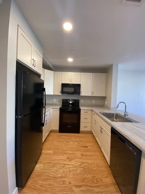 A black refrigerator is in a kitchen with white cabinets.