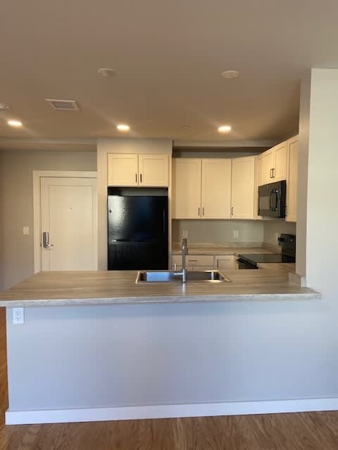 A kitchen with a black refrigerator and white cabinets.