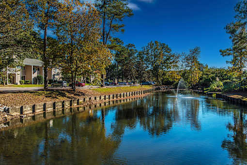 A serene pond with a fountain in the middle surrounded by trees and buildings.