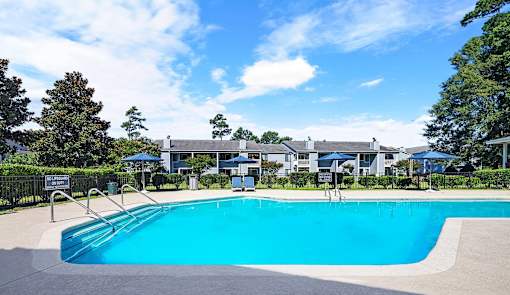 A swimming pool surrounded by trees and a building in the background.