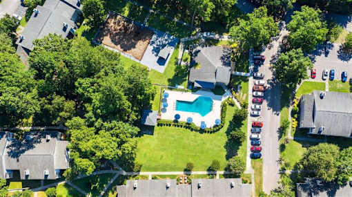 A bird's eye view of a residential area with houses, a swimming pool, and parked cars.