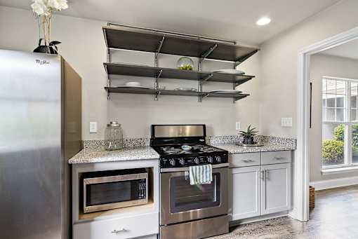 A modern kitchen with a stainless steel refrigerator, microwave, oven, and shelves above the counter.